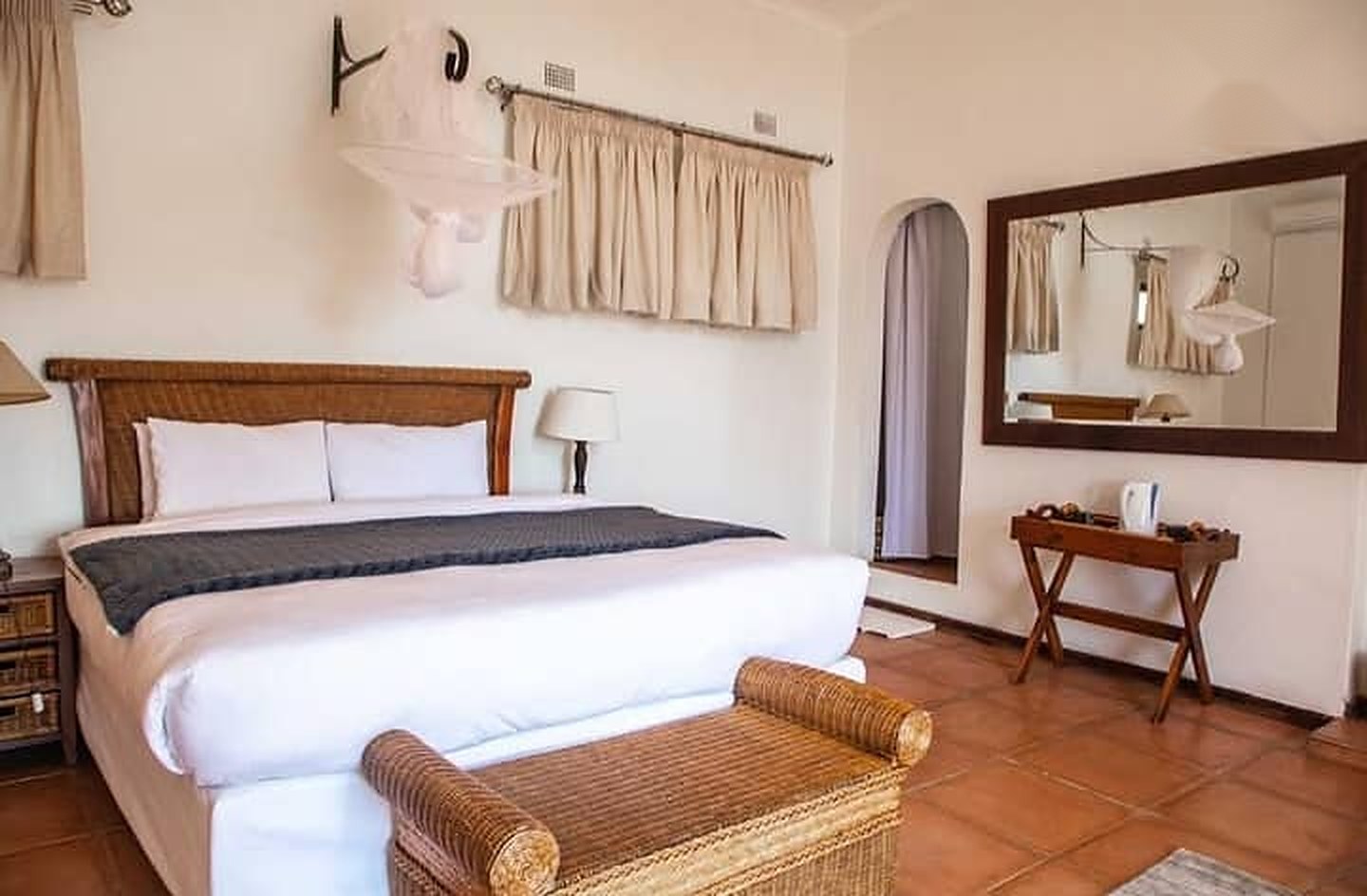 Bedroom with a large bed, wicker bench, mosquito net and a tiled floor
