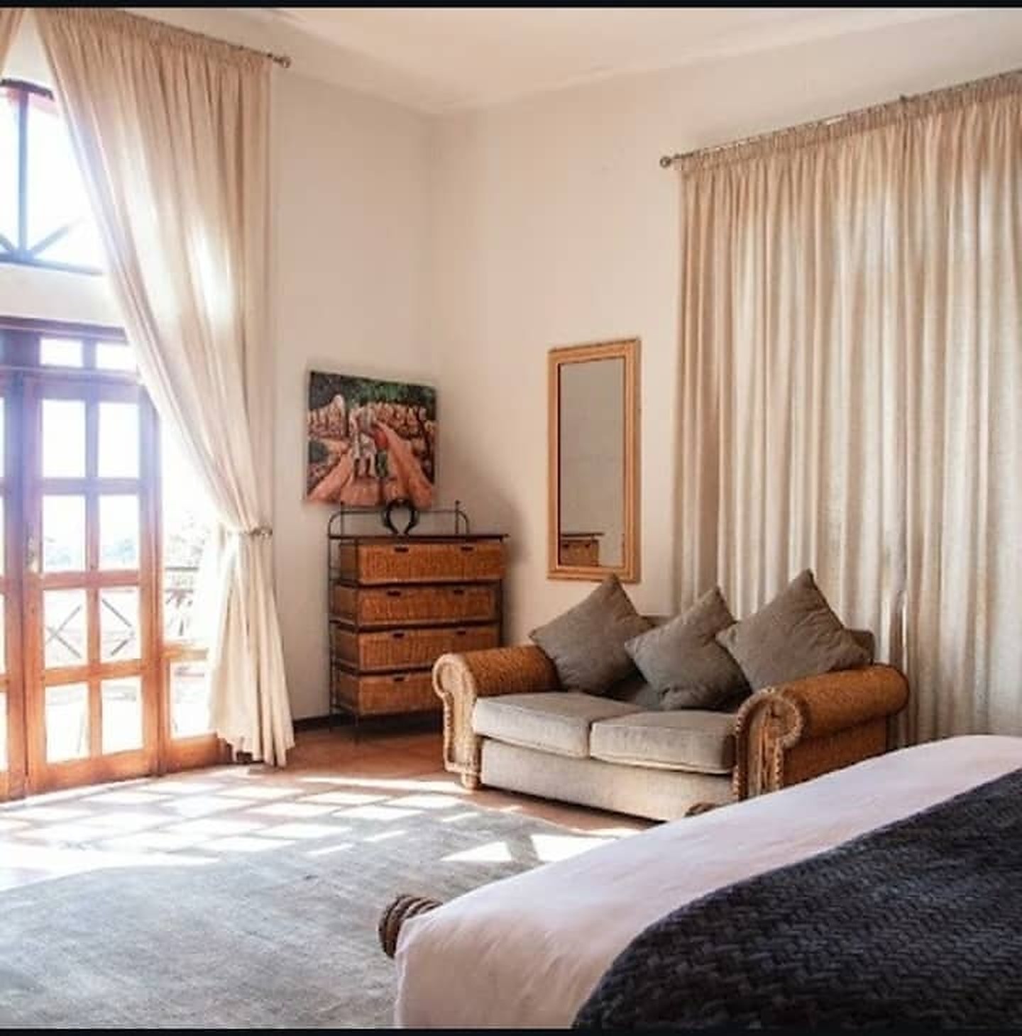 Sunlit room with a wicker sofa, tall balcony doors and cream curtains